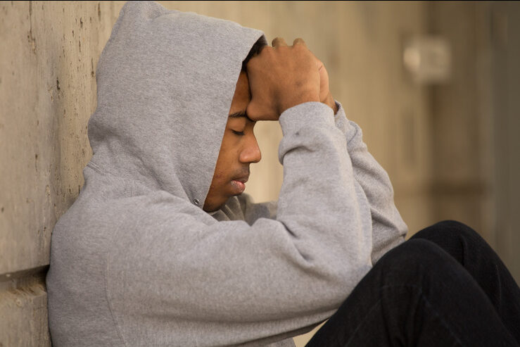 Jeune personne assise contre le mur, la tête dans les mains