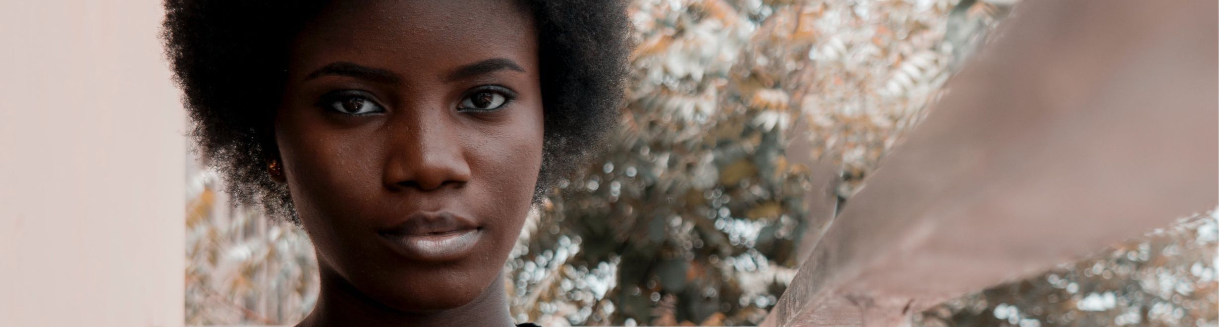 Une jeune personne à l'extérieur faisant directement face à la caméra, avec des arbres flous en arrière-plan.